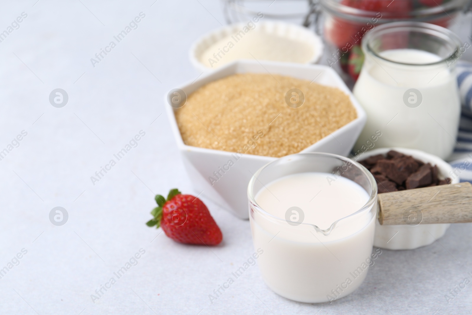 Photo of Different ingredients for panna cotta. Milk, sugar, vanilla, chocolate and strawberries on white table, closeup. Space for text