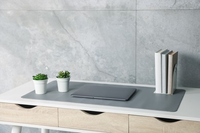 Photo of Stylish workplace with laptop and grey mousepad on white table indoors. Space for text