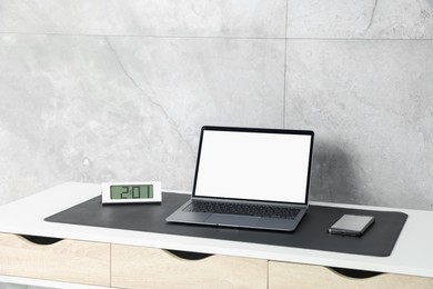 Photo of Stylish workplace with laptop and black mousepad on white table indoors. Space for text