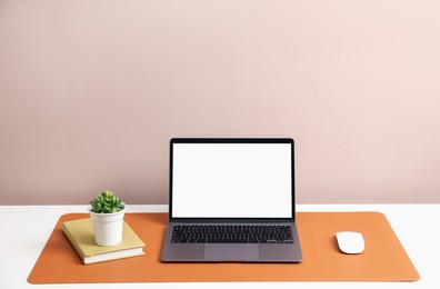 Photo of Stylish workplace with laptop and orange mousepad on white table indoors. Space for text