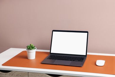 Photo of Stylish workplace with laptop and orange mousepad on white table indoors. Space for text