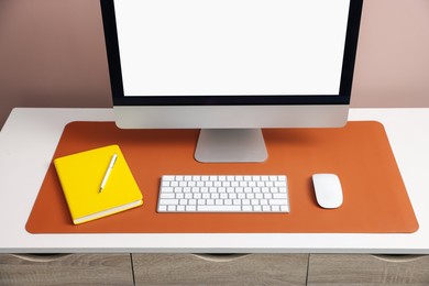 Photo of Stylish workplace with computer and orange mousepad on white table indoors, closeup