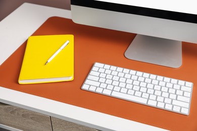 Photo of Stylish workplace with computer and orange mousepad on white table indoors, closeup