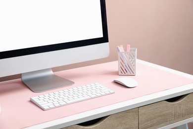 Photo of Stylish workplace with computer and pink mousepad on white table indoors, closeup. Space for text