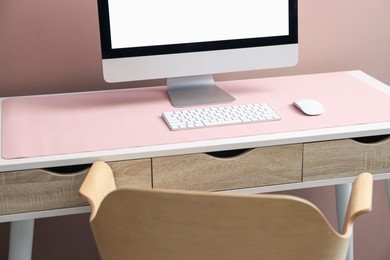Photo of Stylish workplace with computer and pink mousepad on white table indoors. Space for text