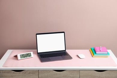 Photo of Stylish workplace with laptop and pink mousepad on white table indoors. Space for text