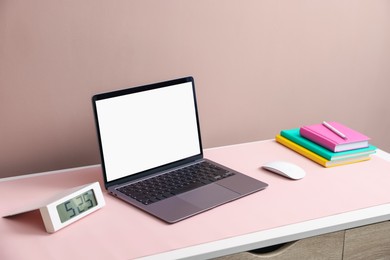 Photo of Stylish workplace with laptop and pink mousepad on white table indoors. Space for text