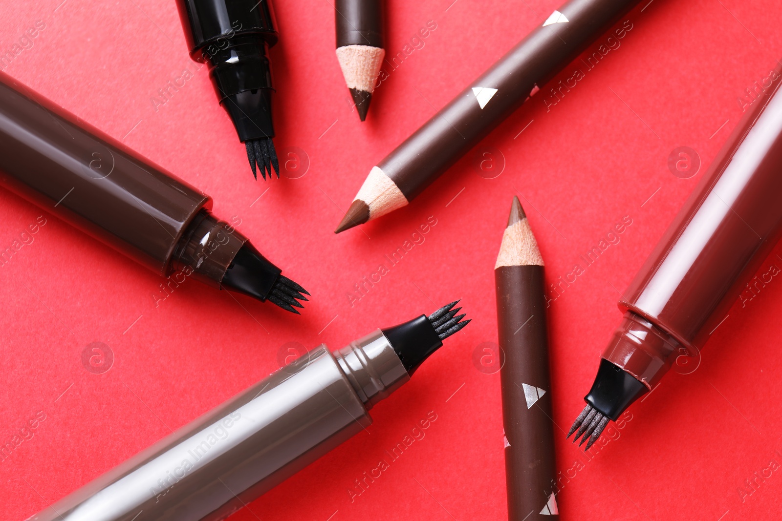 Different eyebrow pencils on red background, flat lay Photo of Different eyebrow pencils on red background, flat lay