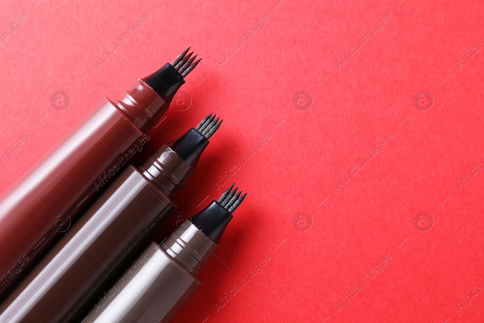 Liquid eyebrow pencils on red background, above view. Space for text Photo of Liquid eyebrow pencils on red background, above view. Space for text