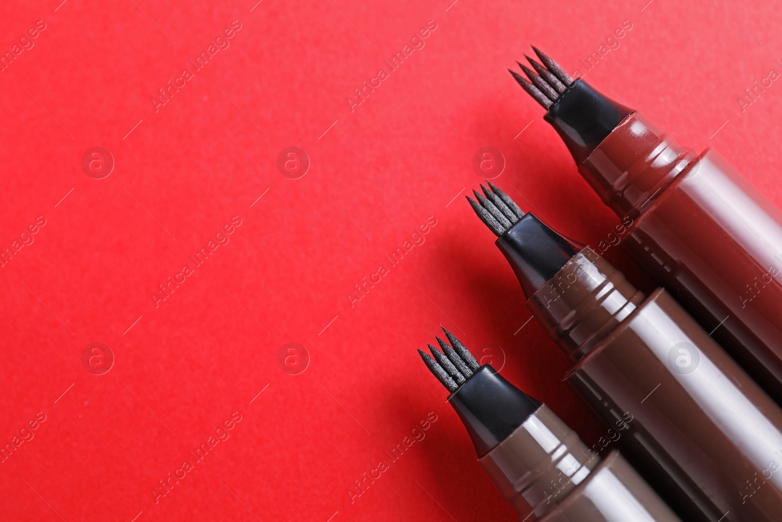 Liquid eyebrow pencils on red background, above view. Space for text Photo of Liquid eyebrow pencils on red background, above view. Space for text