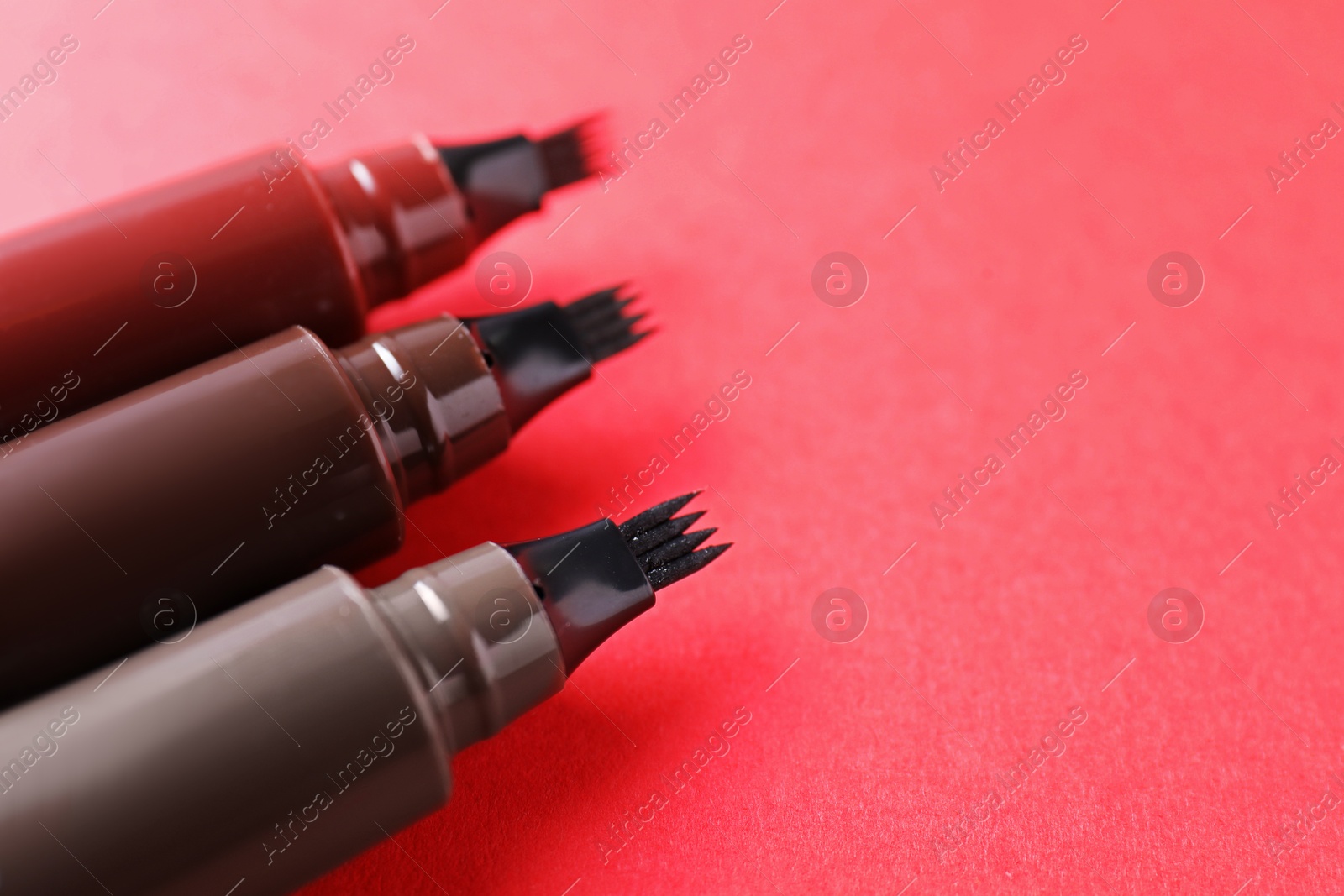 Liquid eyebrow pencils on red background, closeup. Space for text Photo of Liquid eyebrow pencils on red background, closeup. Space for text