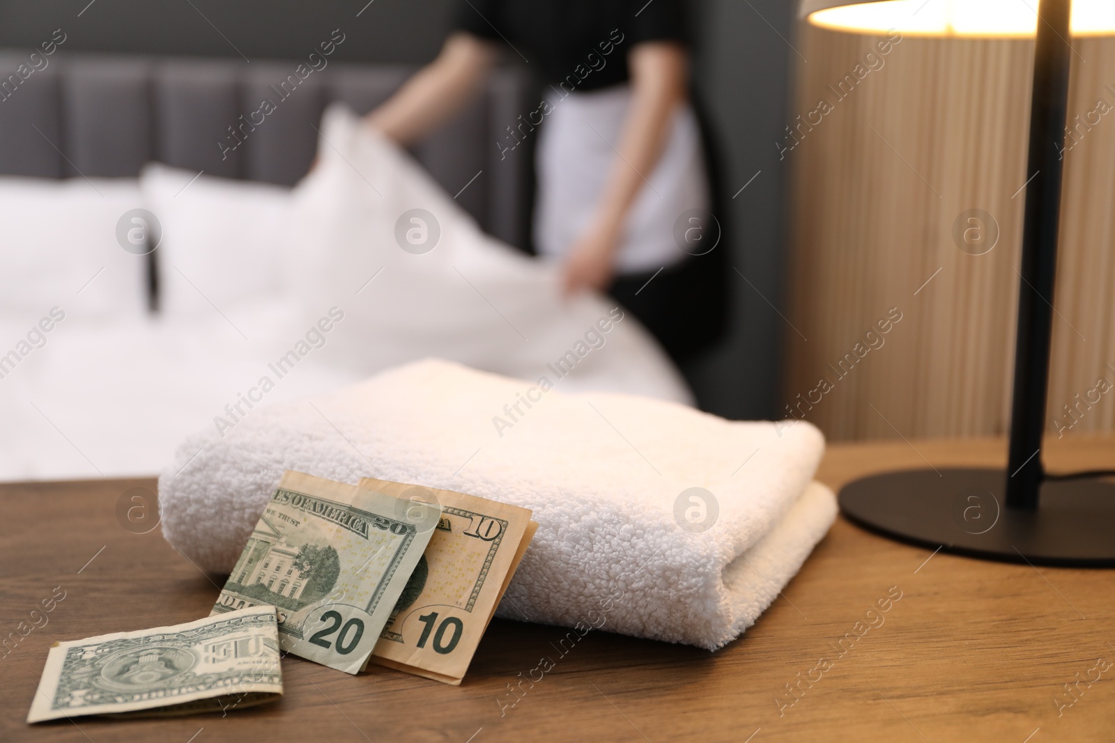 Photo of Chambermaid working in hotel room, focus on tips and towel on wooden nightstand