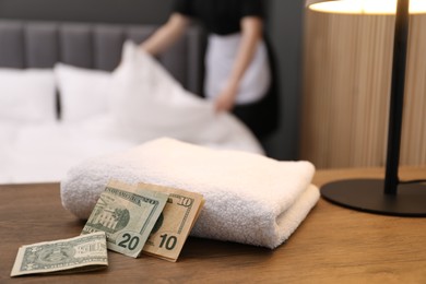 Photo of Chambermaid working in hotel room, focus on tips and towel on wooden nightstand