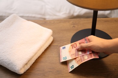 Photo of Woman putting tips on wooden nightstand, closeup