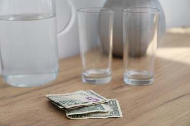 Photo of Tips, glasses and jug of water on wooden nightstand in hotel room, closeup