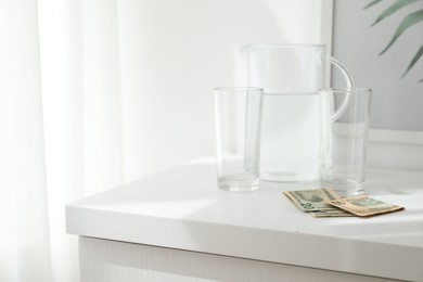 Photo of Tips, glasses and jug of water on white nightstand in hotel room