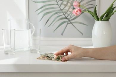 Photo of Woman taking tips from white counter in hotel room, closeup. Gratuity for work