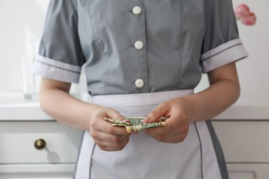 Photo of Chambermaid counting tips leaning chest of drawers in hotel room, closeup. Gratuity for work