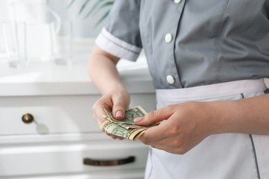 Photo of Chambermaid counting tips leaning chest of drawers in hotel room, closeup. Gratuity for work