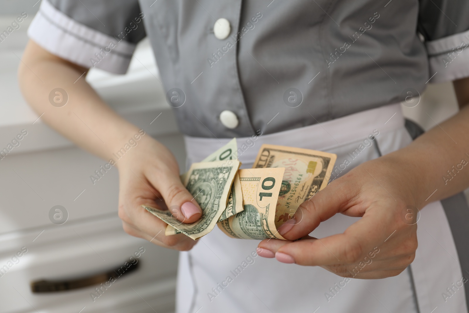 Photo of Chambermaid counting tips leaning chest of drawers in hotel room, closeup. Gratuity for work