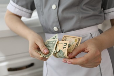 Photo of Chambermaid counting tips leaning chest of drawers in hotel room, closeup. Gratuity for work
