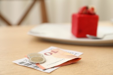 Photo of Tips and receipt on wooden table in restaurant, closeup. Gratuity for work
