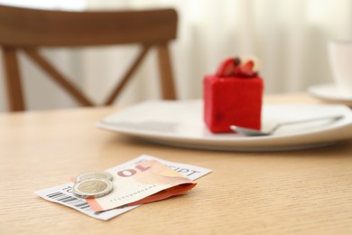 Photo of Tips and receipt on wooden table in restaurant, closeup. Gratuity for work
