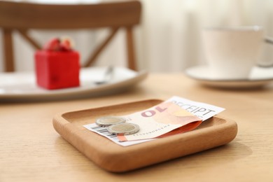 Photo of Tips and receipt on wooden table in restaurant, closeup. Gratuity for work