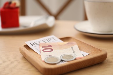 Photo of Tips and receipt on wooden table in restaurant, closeup. Gratuity for work