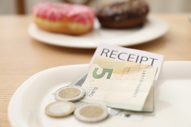 Photo of Tips and receipt on wooden table in restaurant, closeup. Gratuity for work