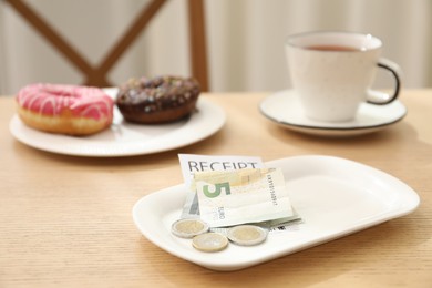 Photo of Tips and receipt on wooden table in restaurant, closeup. Gratuity for work