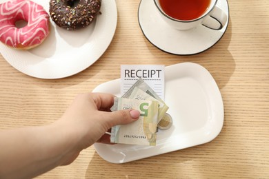 Photo of Woman putting tips onto plate at wooden table, top view