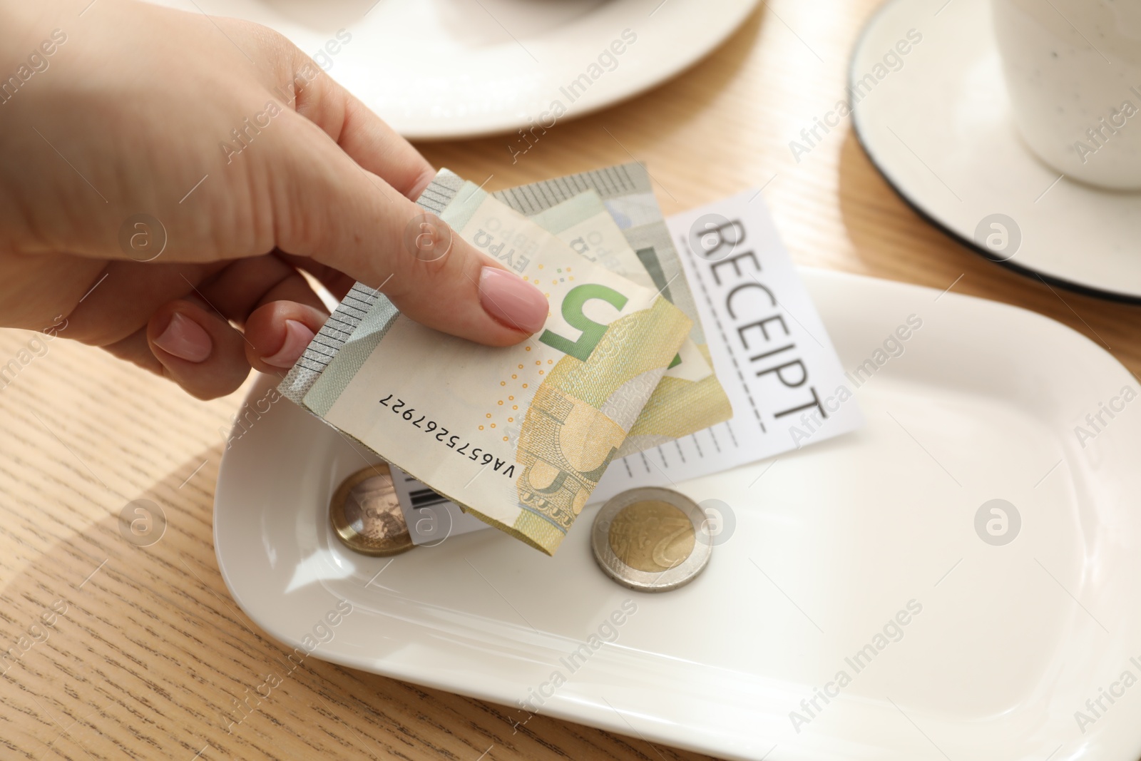 Photo of Woman putting tips onto plate at wooden table in cafe, closeup