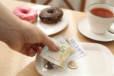 Photo of Woman putting tips onto plate at wooden table in cafe, closeup