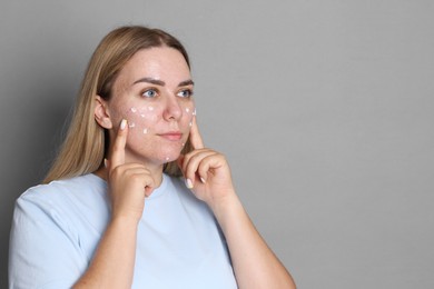 Photo of Woman applying cream onto face on grey background, space for text. Acne treatment