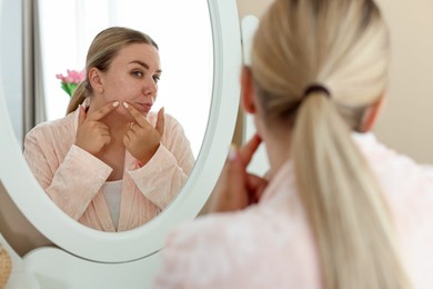 Photo of Woman with acne problem looking in mirror at home