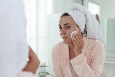 Photo of Woman with acne problem cleaning her face near mirror indoors