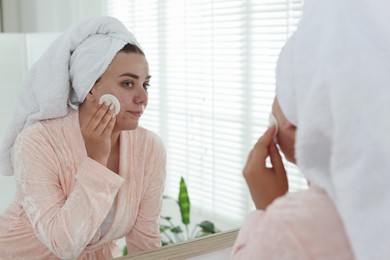 Photo of Woman with acne problem cleaning her face near mirror indoors