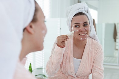 Photo of Woman applying cream onto face near mirror indoors. Acne treatment
