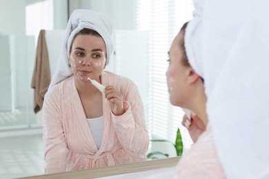 Photo of Woman applying cream onto face near mirror indoors. Acne treatment