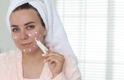 Photo of Woman applying cream onto face in bathroom, space for text. Acne treatment