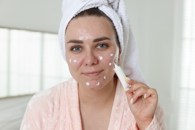 Photo of Woman applying cream onto face in bathroom. Acne treatment