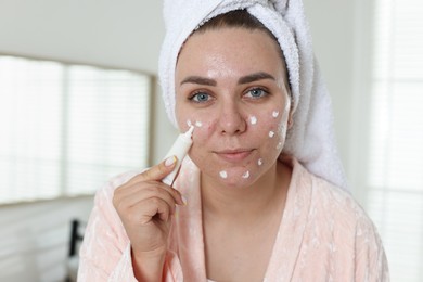 Photo of Woman applying cream onto face in bathroom. Acne treatment