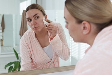 Photo of Woman applying cream onto face near mirror indoors. Acne treatment