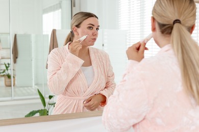 Photo of Woman applying cream onto face near mirror indoors. Acne treatment
