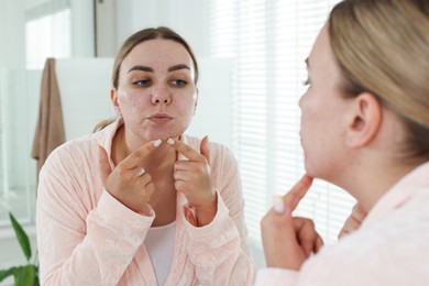 Photo of Woman popping pimple near mirror in bathroom. Acne problem