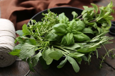 Photo of Different fresh green herbs in bowl and twine on wooden table, closeup