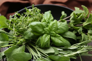 Photo of Different fresh green herbs in bowl on table, closeup