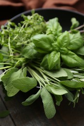 Photo of Different fresh green herbs in bowl on wooden table, closeup