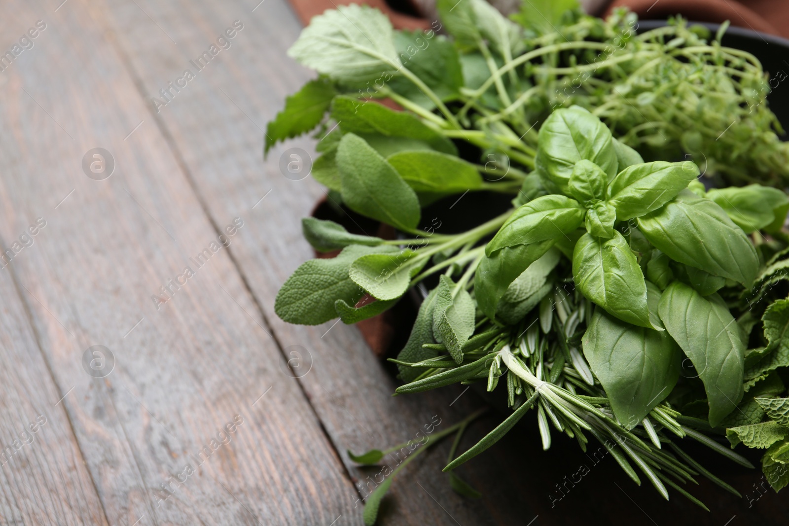 Different fresh green herbs in bowl on wooden table, closeup. Space for text Photo of Different fresh green herbs in bowl on wooden table, closeup. Space for text